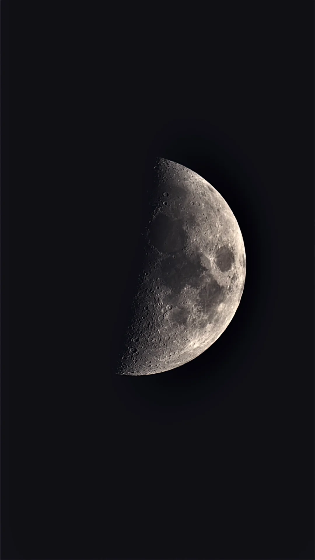 The Moon, partly lit, its craters sharp along the line between day and night