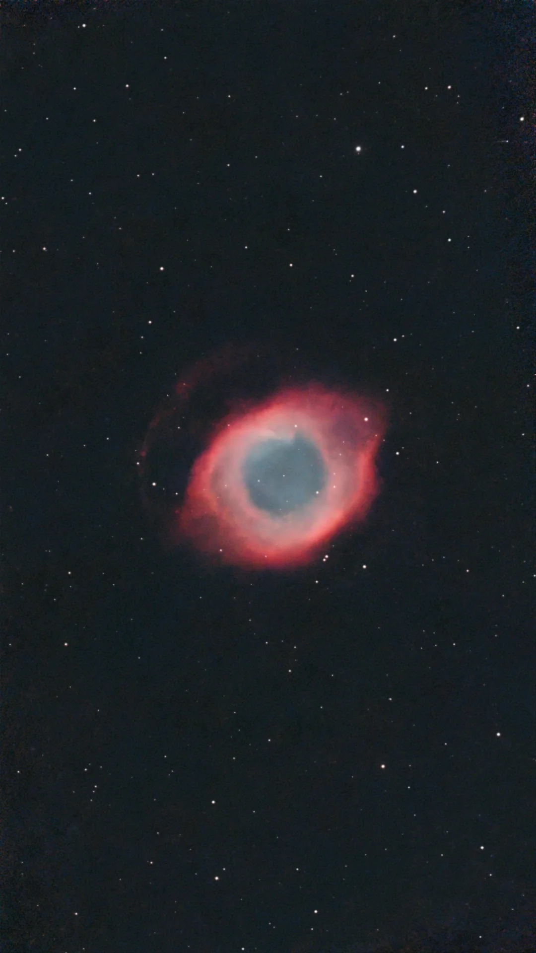 The Helix Nebula: a red ring with a blue centre in a field of stars