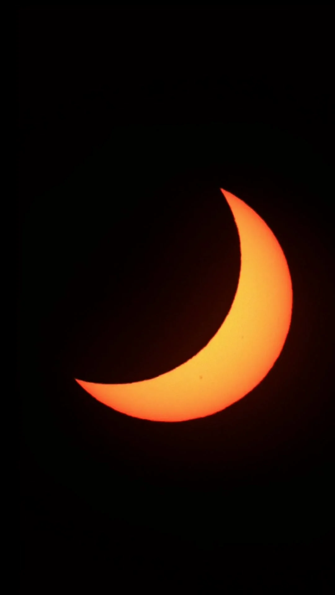A thick orange crescent of the Sun against black, the Moon covering its upper left
