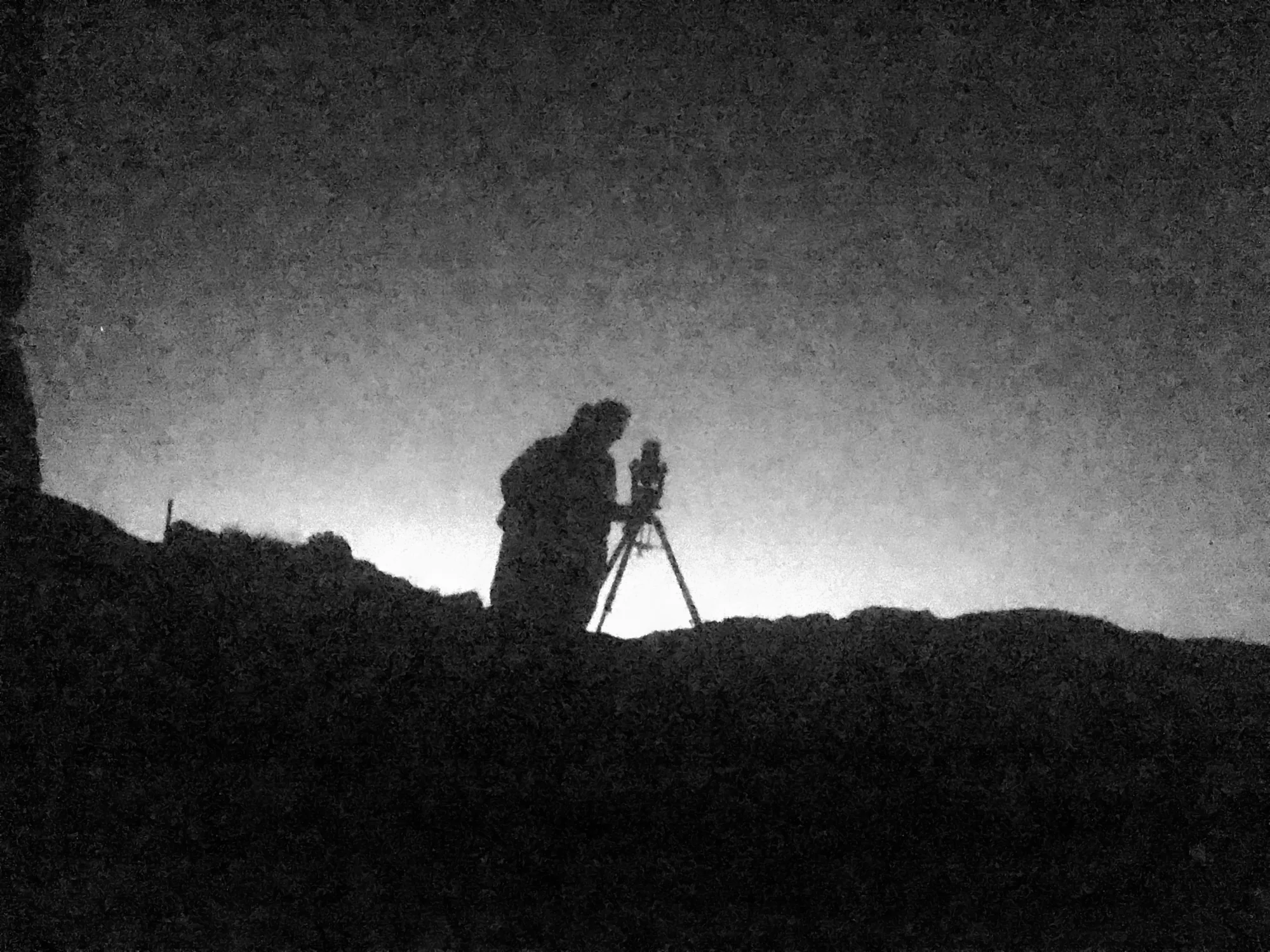 Silhouette of a person at a telescope against a bright sky