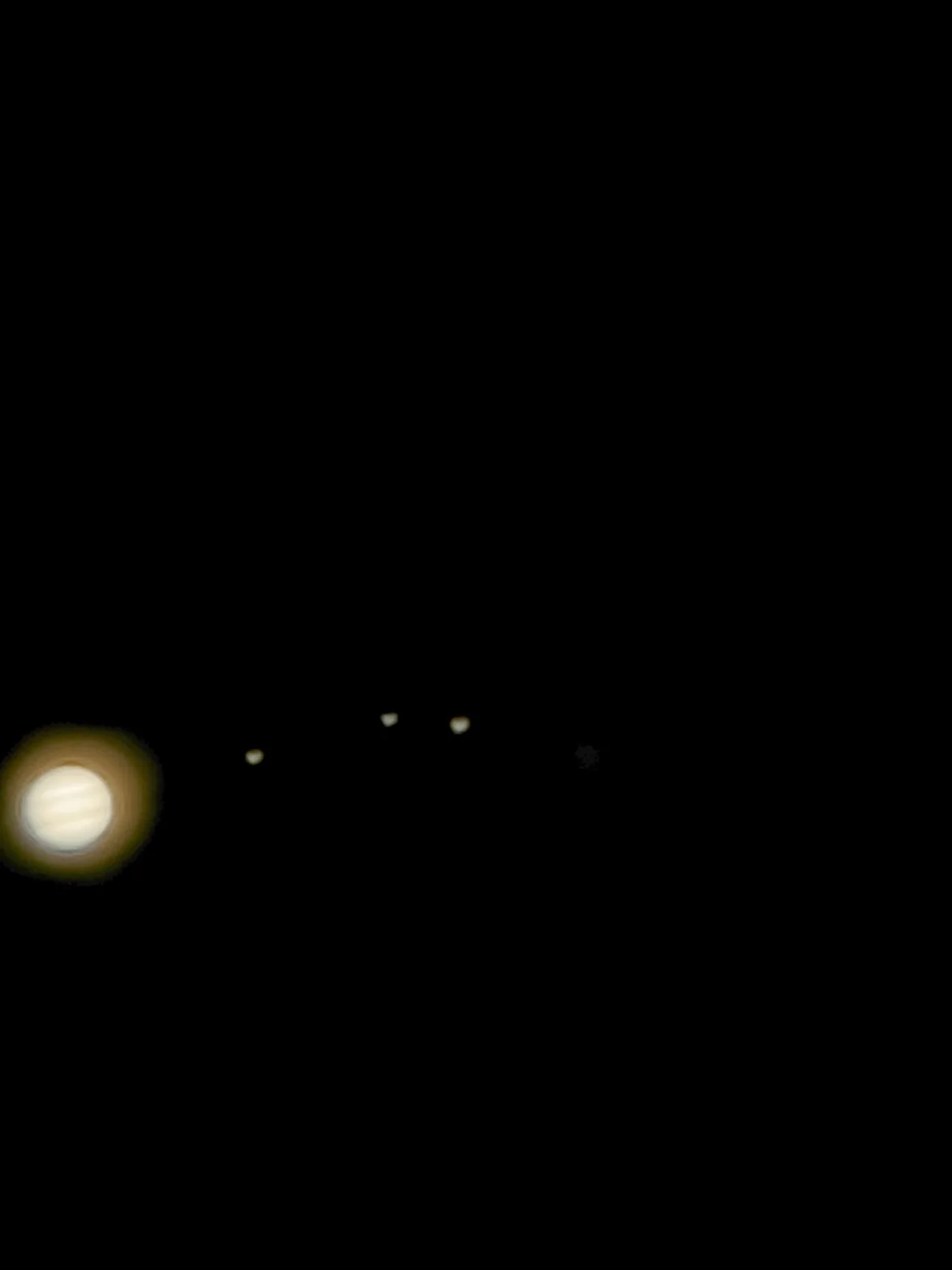 Jupiter with faint cloud bands at the left edge and three moons in a row to its right
