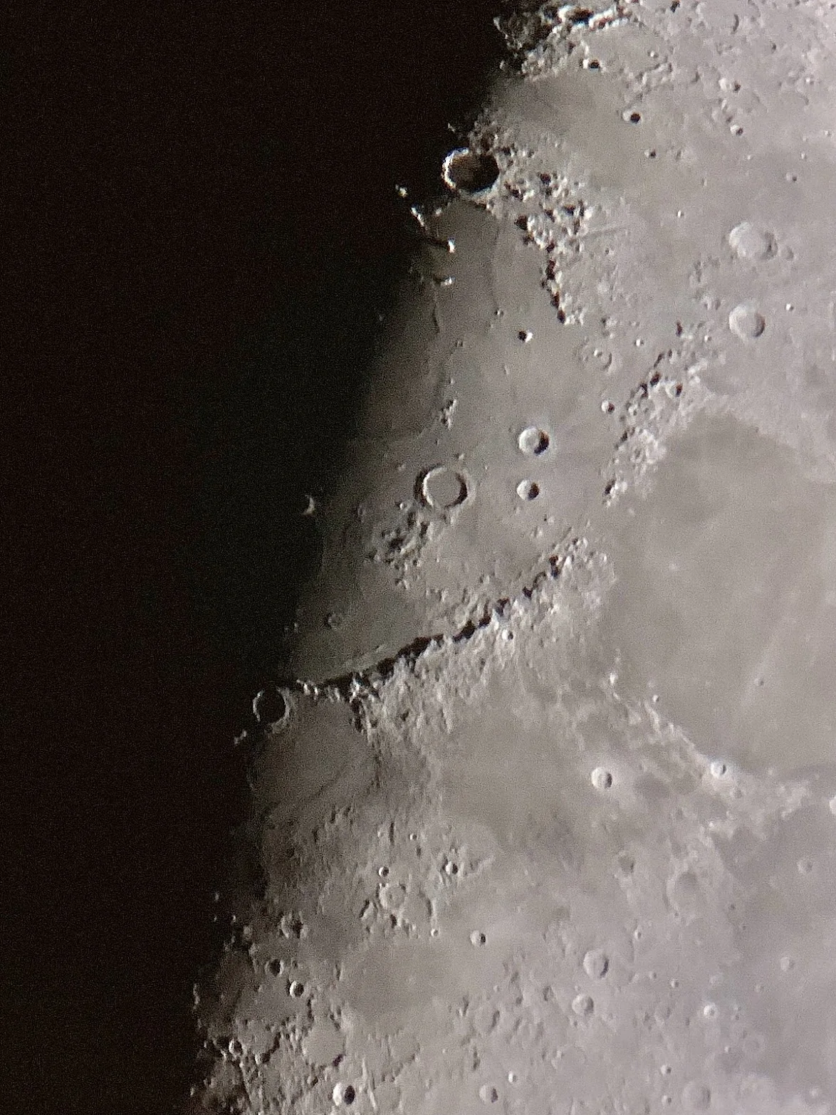 The Moon's terminator in close-up, a curved mountain range and craters in raking light beside the dark edge