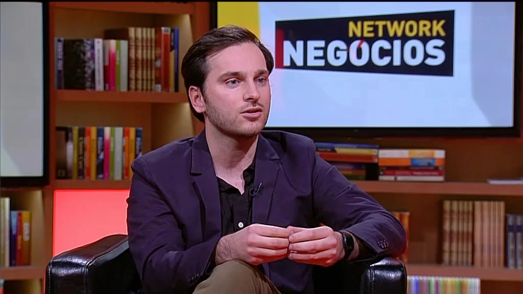 João Montenegro in a dark blazer, answering a question on the Network Negócios set