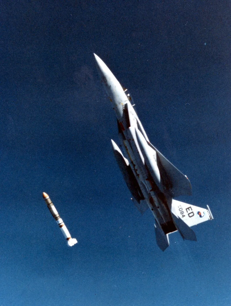 An F-15 fighter climbing steeply into a blue sky, the missile just released below it
