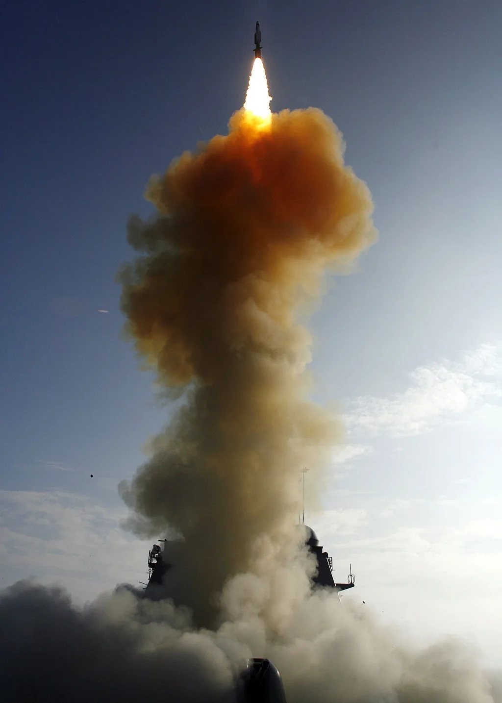 A missile rising from a warship on a tall column of orange-brown smoke