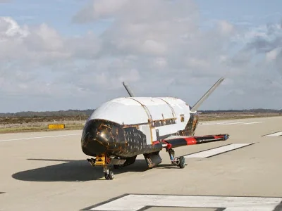 The X-37B, a small white and black spaceplane, parked on a runway