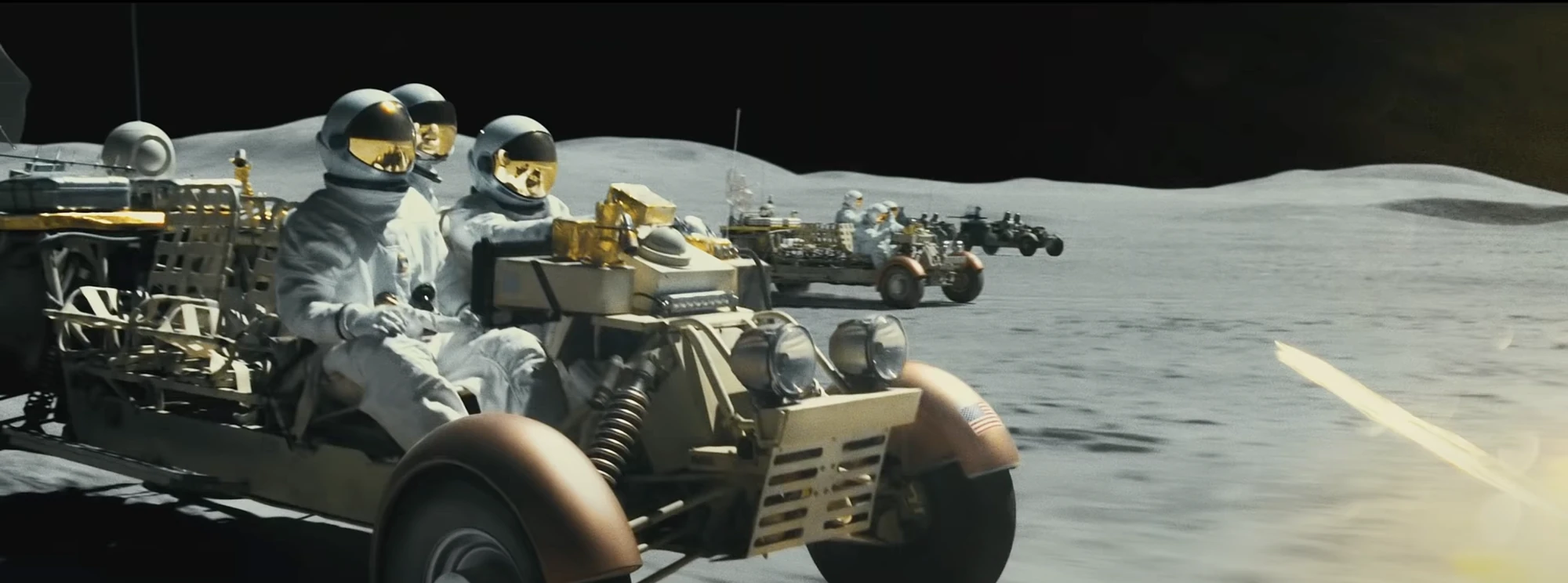 Astronauts riding open lunar rovers in a line across grey ground, with a dark vehicle at the far end and a yellow streak at the right